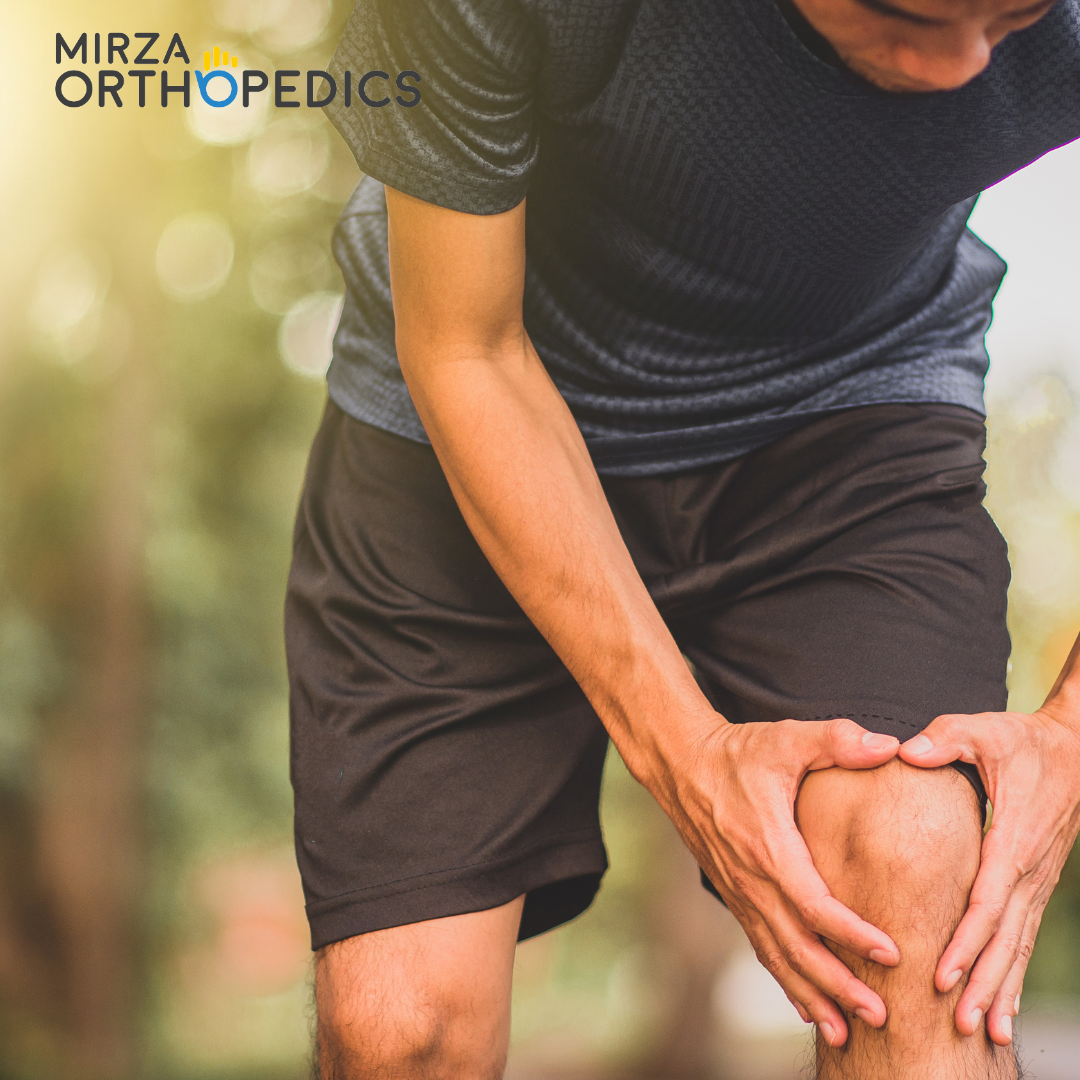 Person holding their knee in discomfort while standing outdoors.