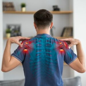 A man in a blue shirt stands with his back to the camera, touching his shoulders. An illustrated overlay shows his spine, with red highlights indicating shoulder pain—an issue an orthopedist in Blue Point, NY could expertly address.